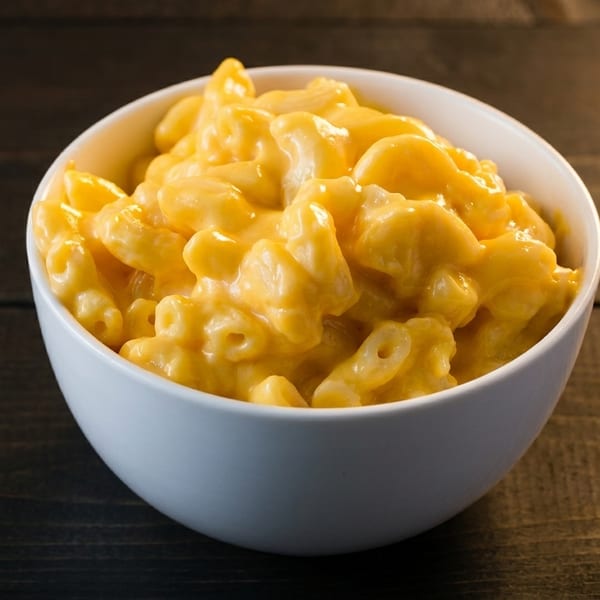 A white bowl filled with creamy, golden macaroni and cheese sits on a dark wooden table.