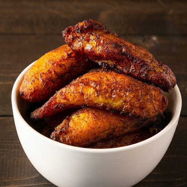 A white bowl filled with golden-brown fried plantains, resting on a dark wooden surface.