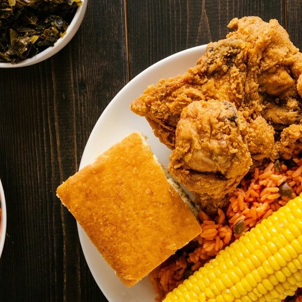 Fried chicken, red rice, cornbread, and collard greens on a dark wooden table.