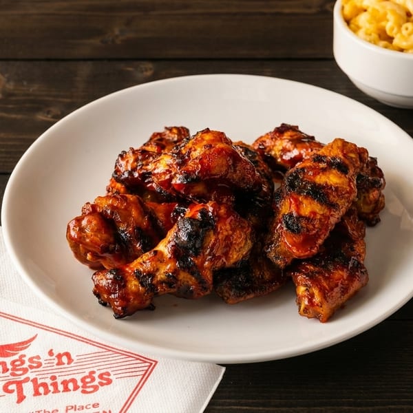 A plate of grilled chicken wings with barbecue sauce, a side of mac and cheese, and a napkin.