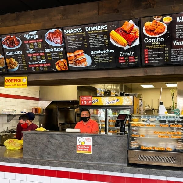 Restaurant interior with menu boards, two employees behind a counter, and a soda fountain.