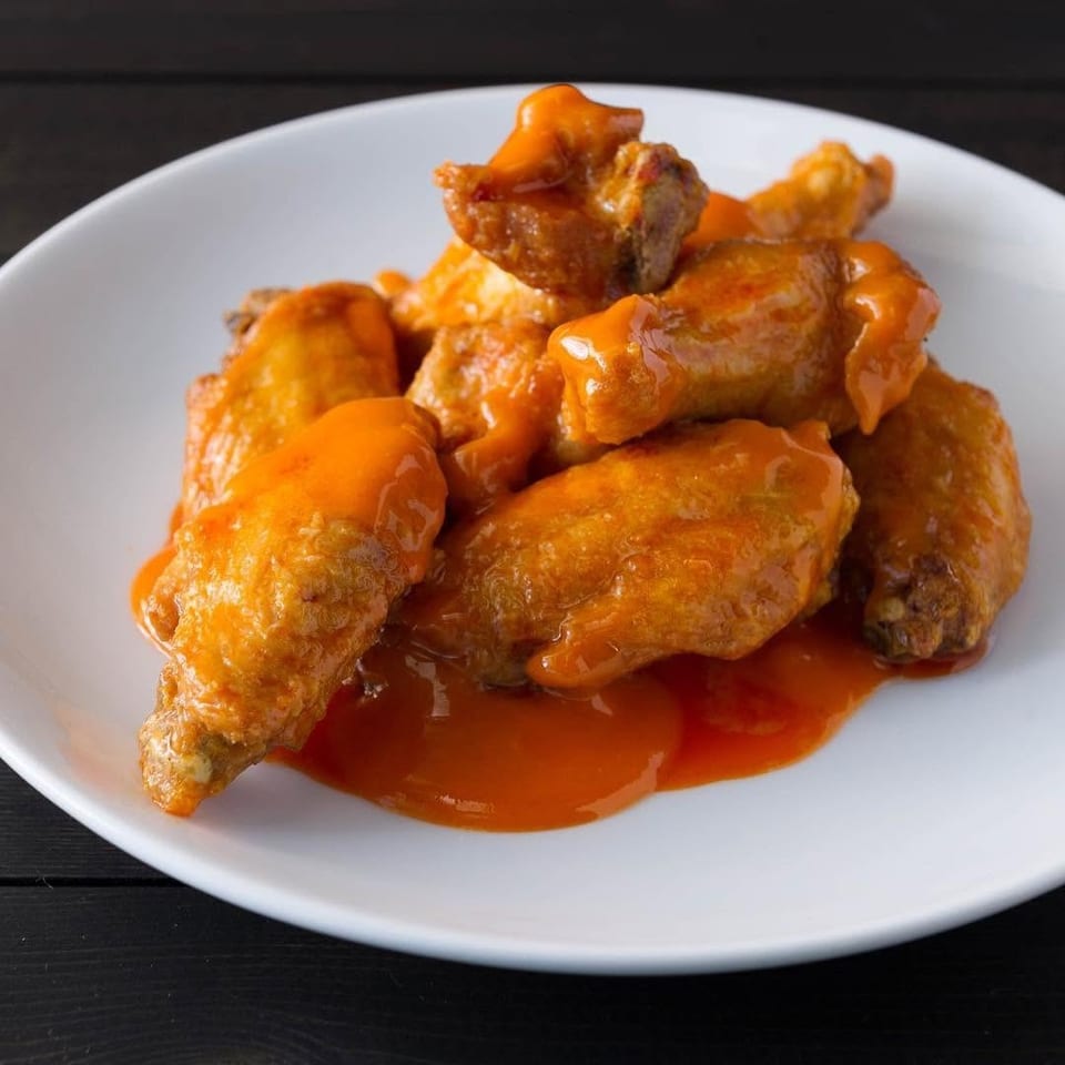 Crispy chicken wings coated in glossy orange sauce, piled on a white plate over a dark wooden table.