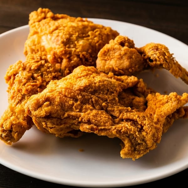 Crispy golden-brown fried chicken pieces on a white plate, set against a dark wooden table.